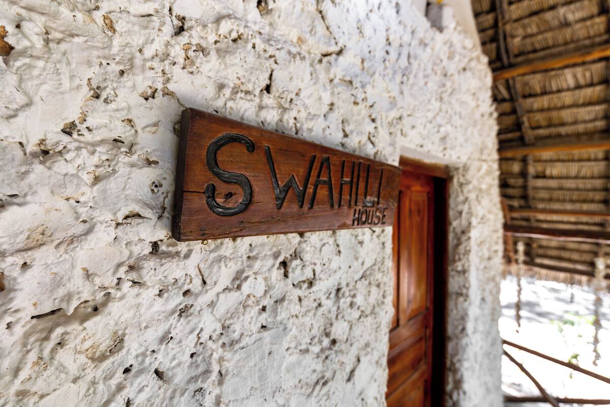 Un letrero de madera con el texto 'SWAHILI HOUSE' colocado en una pared con textura.