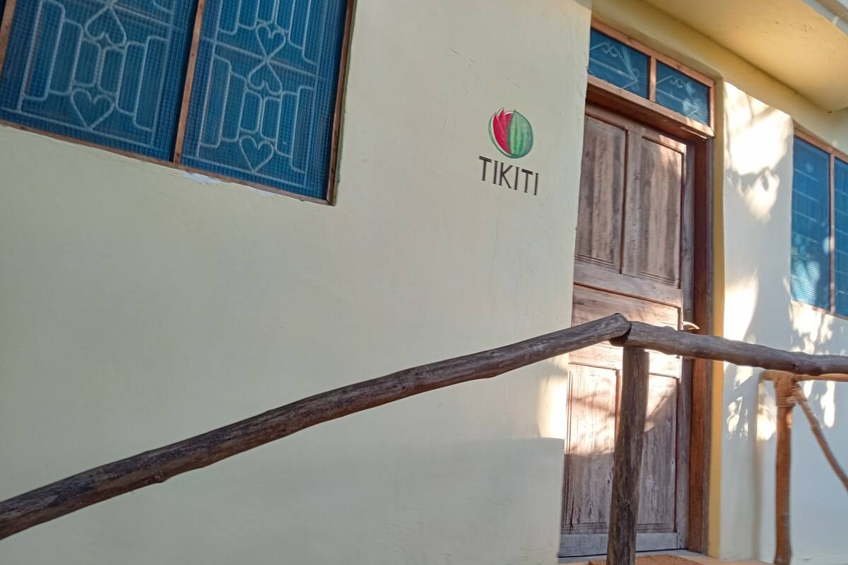 Entrada de un edificio con puerta de madera, reja de metal y pared con un logotipo y la palabra "TIKITI".