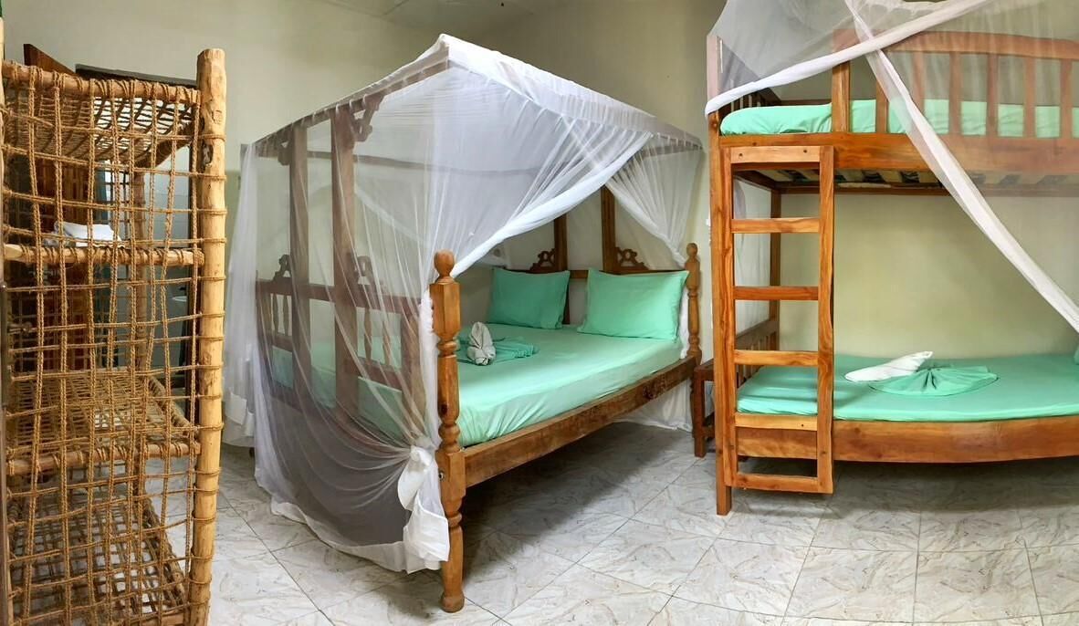 A room with a wooden bed with a canopy, a bunk bed, and a woven rattan chair.
