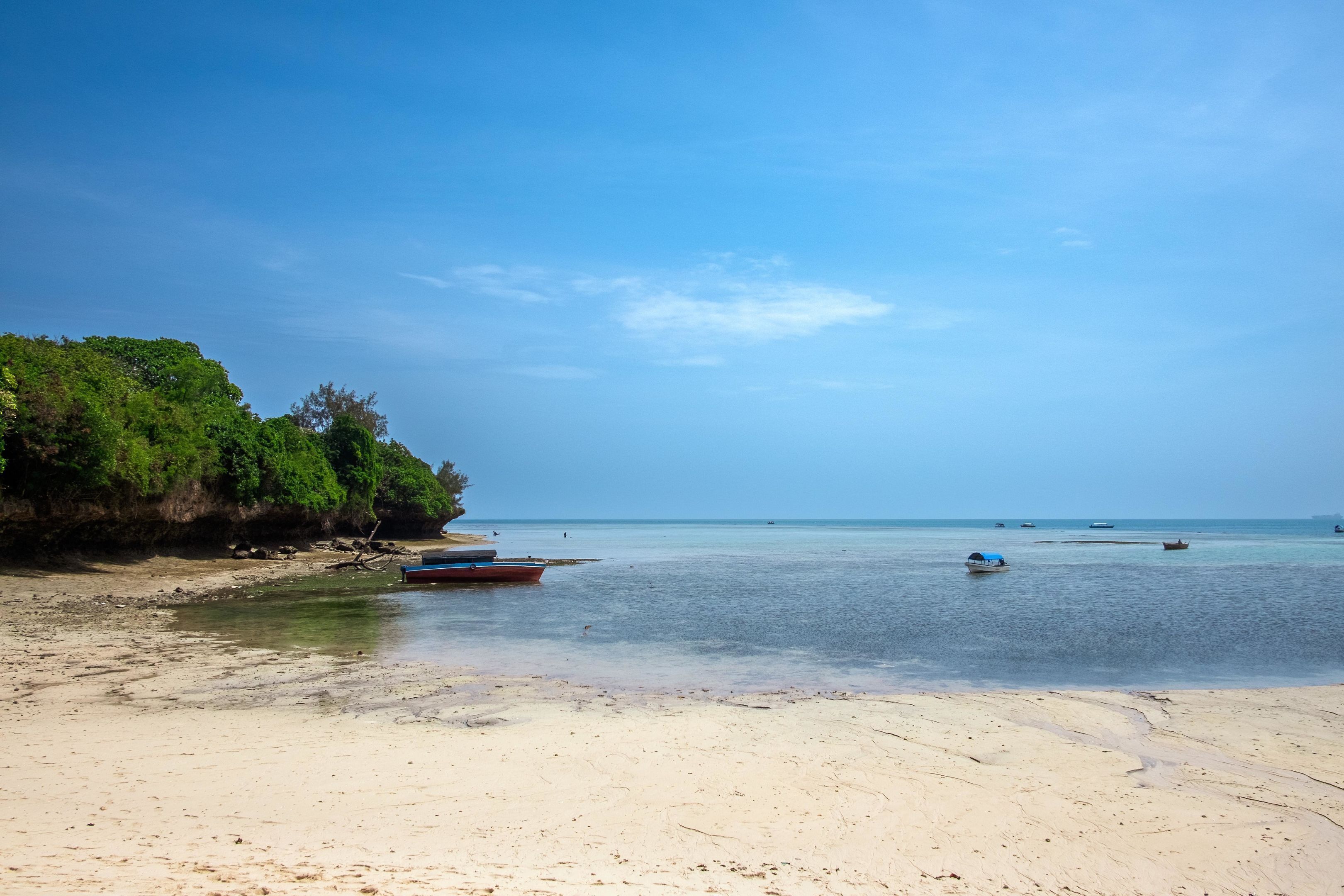 A beach with boats, clear water, and a sandy shore.