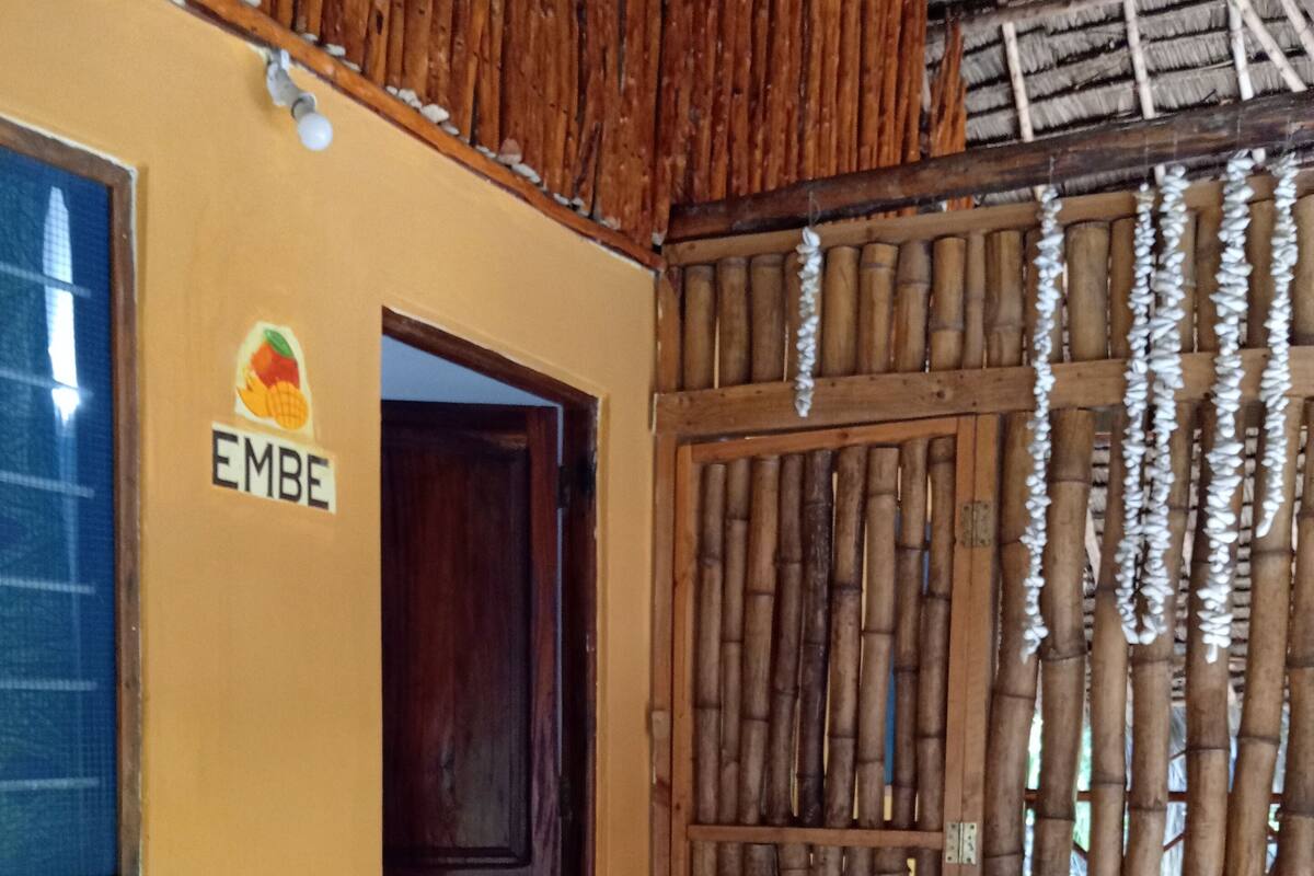 Una habitación rústica con una puerta de madera que dice "EMBE", un panel de bambú tejido y una mesa de madera con sillas.