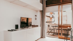 A modern living room with a flat-screen TV, a 'Welcome' sign, and a dining area with a table and chairs.