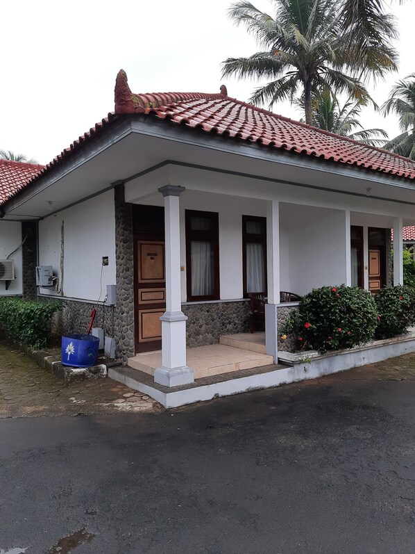 A two-story house with a tiled roof, a porch with columns, and a stone wall. - Resort Prima Anyer (Cinangka)