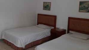 A room with two single beds, each with a wooden headboard, a small bedside table, and a wall-mounted picture. - Resort Prima Anyer (Cinangka)