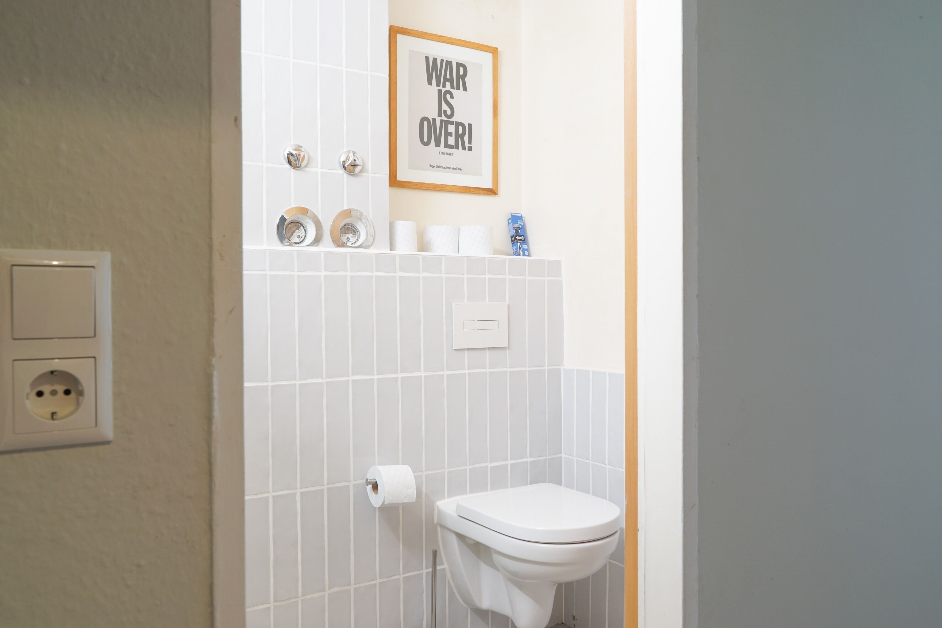Um banheiro com vaso sanitário, uma placa emoldurada na parede e um rolo de papel higiênico.