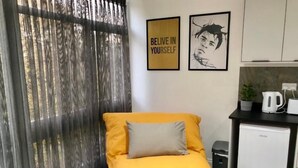 A modern room with a yellow sofa, a small kitchen area with a kettle, and a motivational poster on the wall. - Cosy Flat for 1-3 not far From City Centre (Leicester)