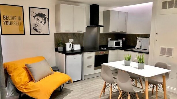 A compact kitchen with white cabinets, a microwave, and a small refrigerator. There is a dining table with chairs and a potted plant. - Cosy Flat for 1-3 not far From City Centre (Leicester)