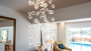 Een moderne woonkamer met een groot raam, een hanglamp en een zwembad dat door het raam zichtbaar is.