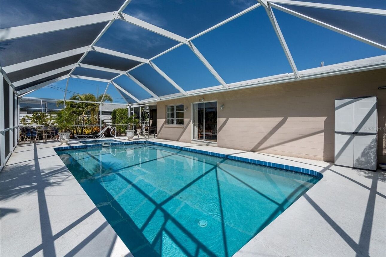 Una piscina con techo de vidrio geométrico, rodeada por un edificio color beige con puerta y ventanas.