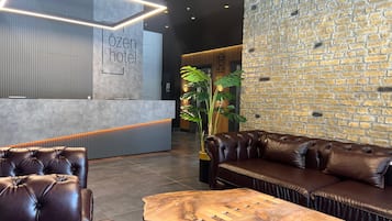 A modern hotel reception area with a stone wall, leather seating, and a wooden coffee table.