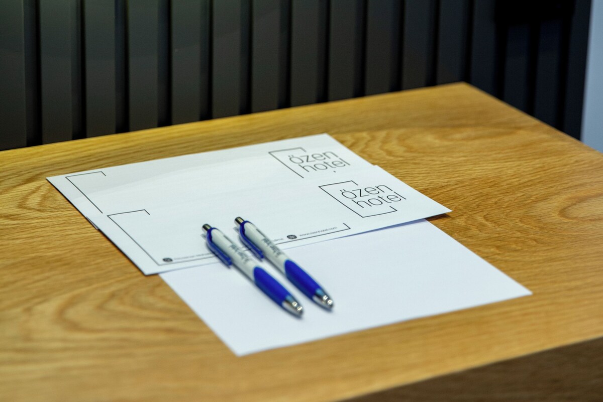 Uma mesa de madeira com uma folha de papel branca, duas canetas e o logotipo de um hotel.