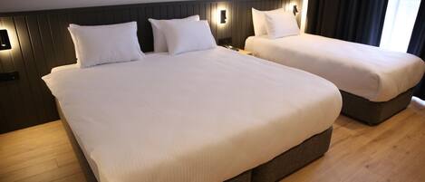 Ein Hotelzimmer mit zwei Betten, Holzboden und einem dunkelbraunen Kopfteil.