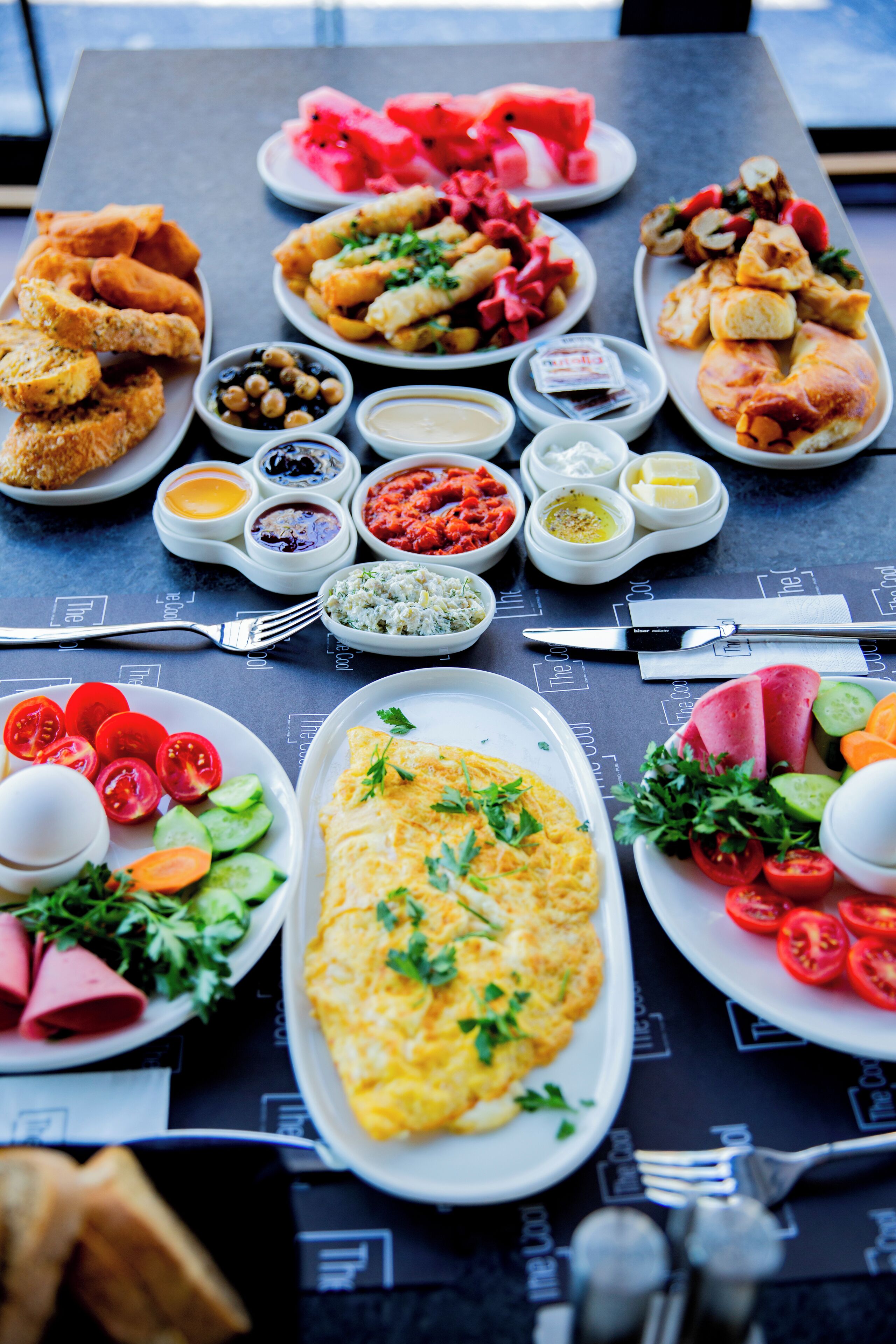 Une table dressée avec divers plats, notamment des salades, de la viande et une grande omelette.