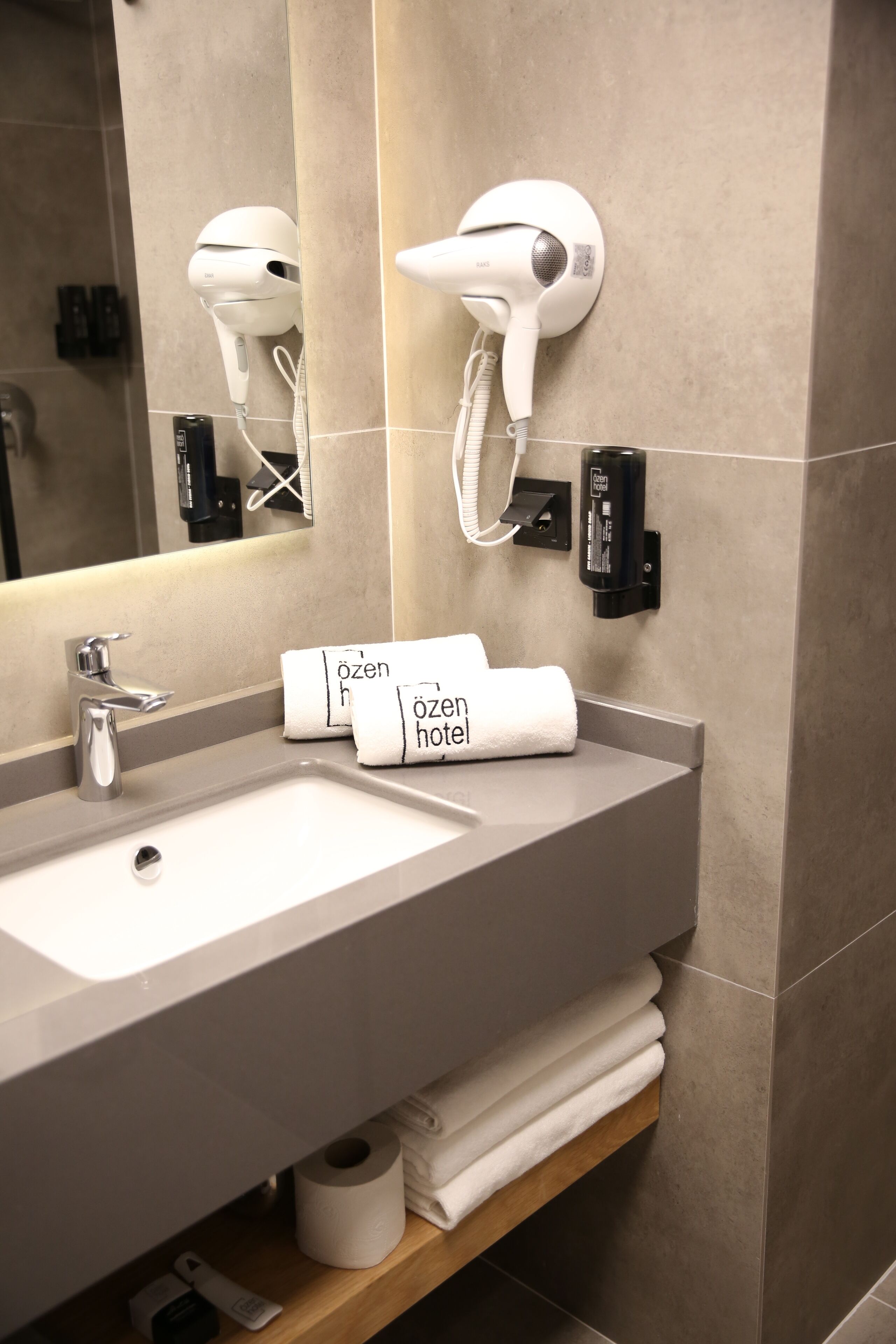 Een hotelbadkamer met een wastafel, handdoekdispenser en een haardroger bevestigd aan de muur.