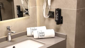 Een hotelbadkamer met een wastafel, handdoekdispenser en een haardroger bevestigd aan de muur.