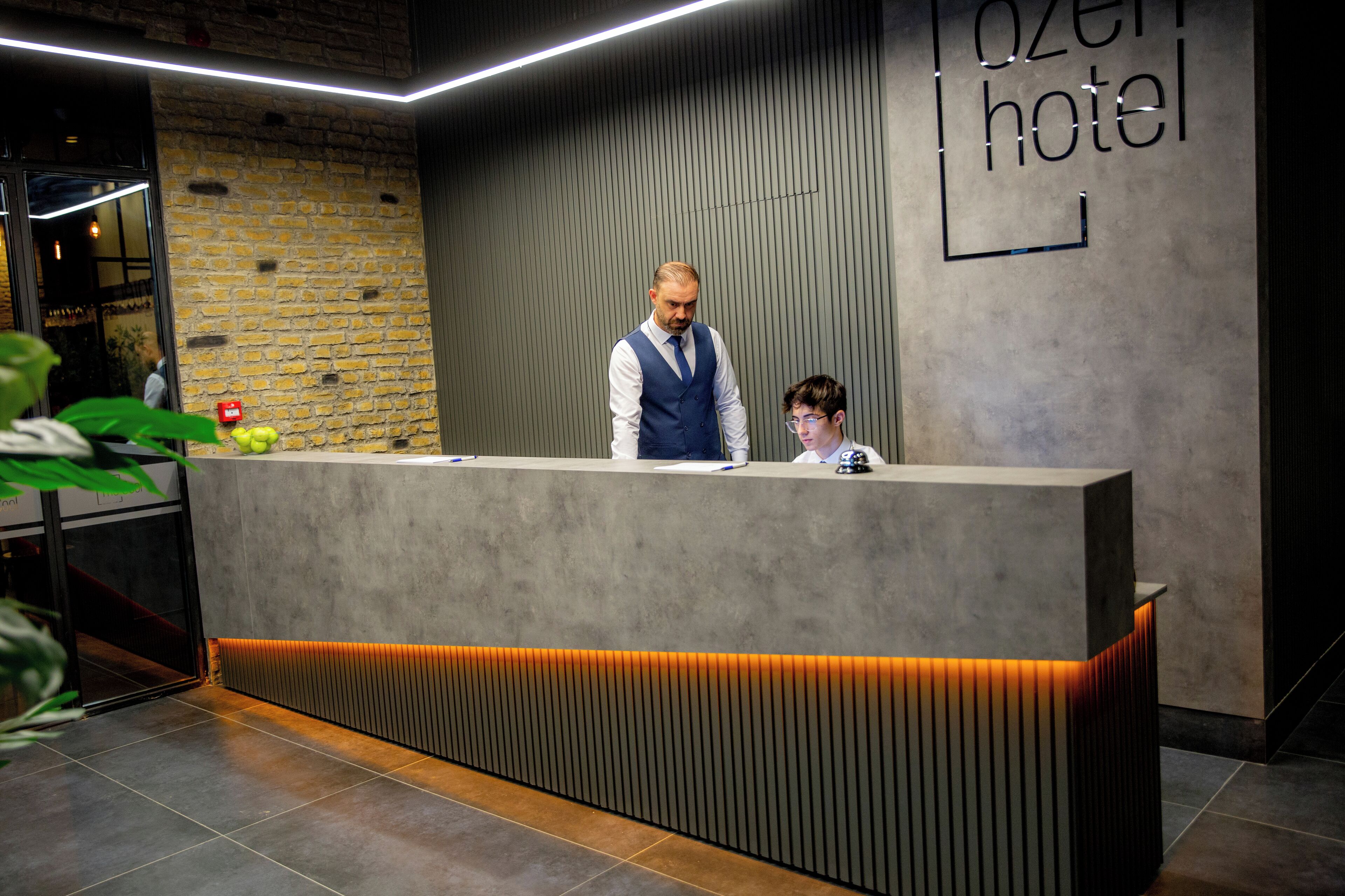 En moderne hotelreception med en murstensvæg, og et skilt der står 'Ozen Hotel'.