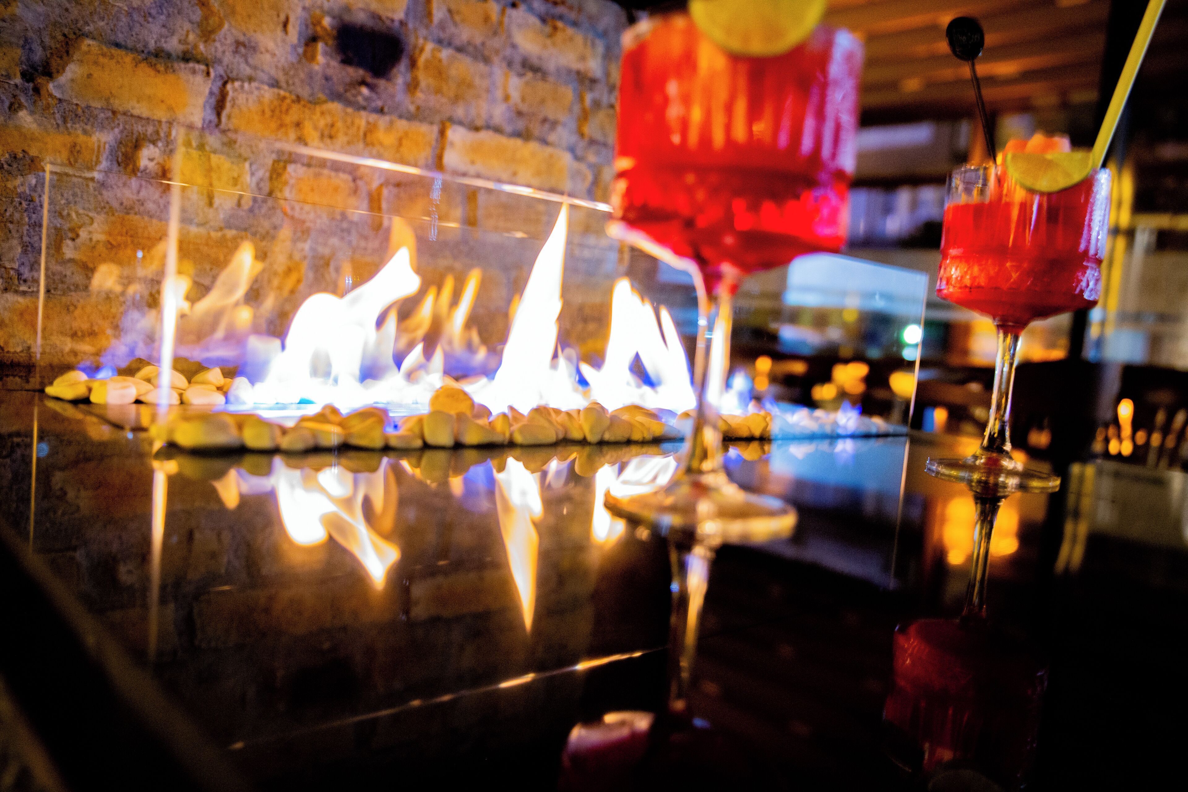 A bar area with a fireplace, a glass of red cocktail, and a reflection on the polished surface.