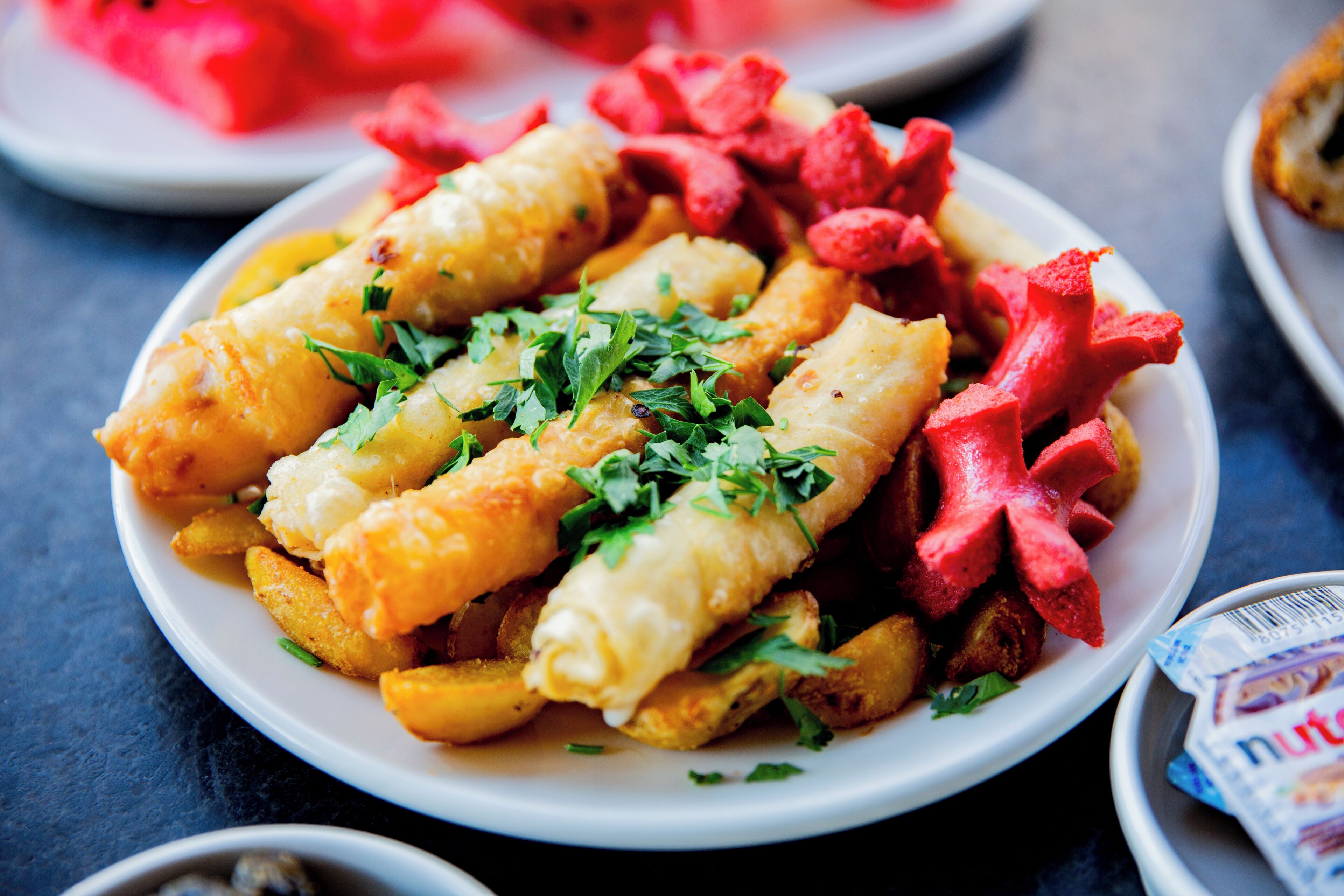 Un plato de comida con pescado, papas fritas y verduras rojas, adornado con hierbas.