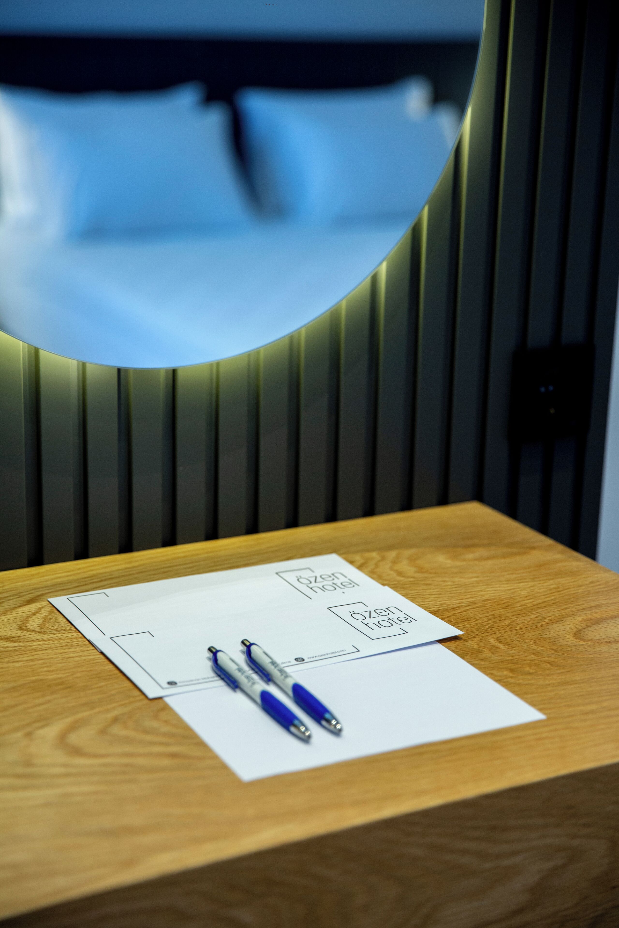Uma mesa de madeira com uma folha de papel branca, duas canetas e o logotipo de um hotel.
