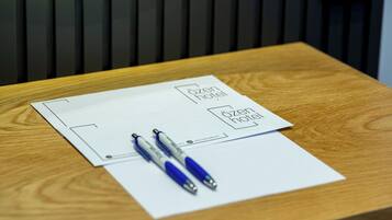 A wooden desk with a white sheet of paper, two pens, and a hotel logo.