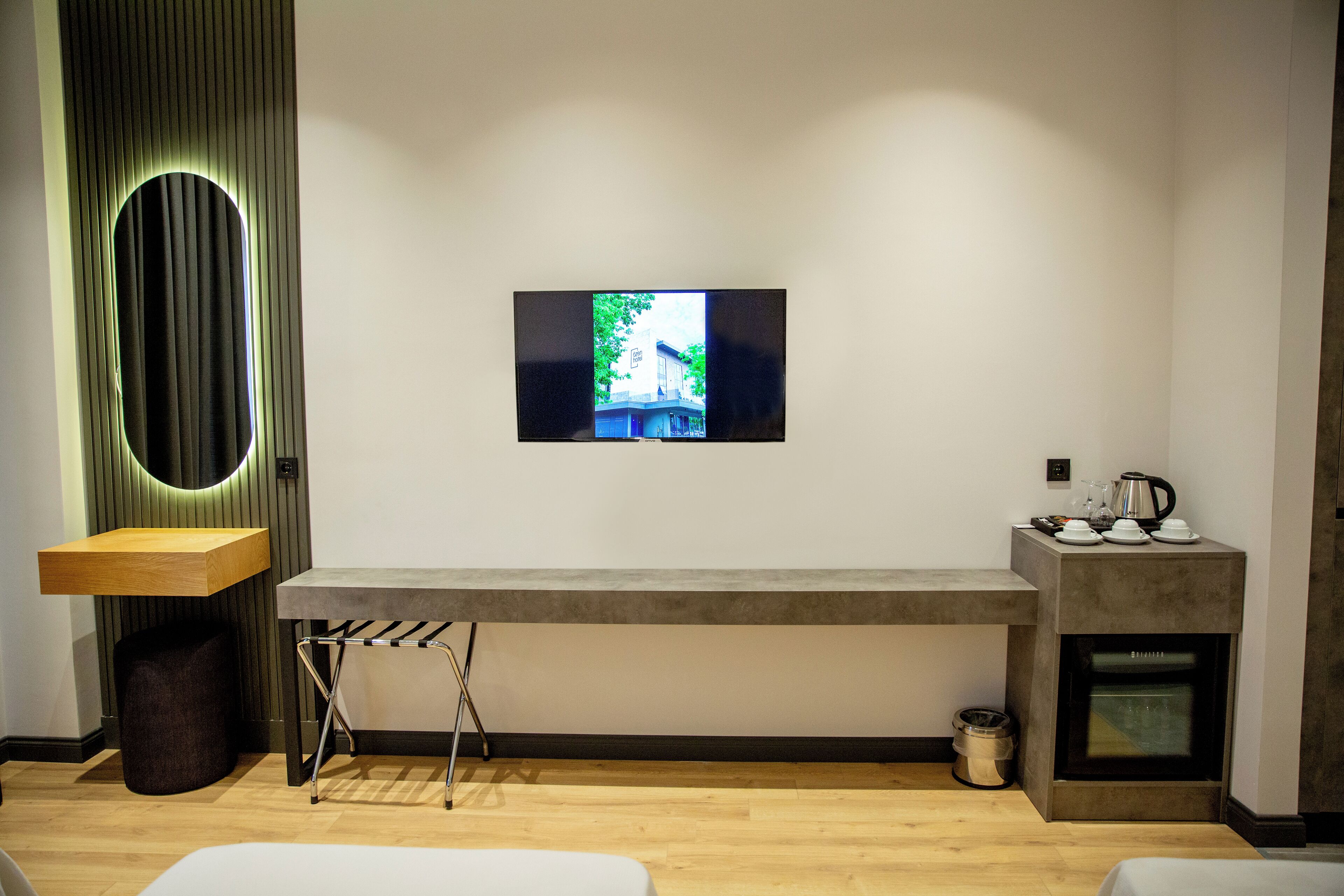 A modern room with a flat-screen TV mounted on the wall, a wooden bench, a small sink, and a built-in oven.