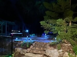 Ein Außenbereich bei Nacht mit Steintreppen, die zu einem Weg führen, umgeben von Bäumen und beleuchtet durch kleine Lichter.