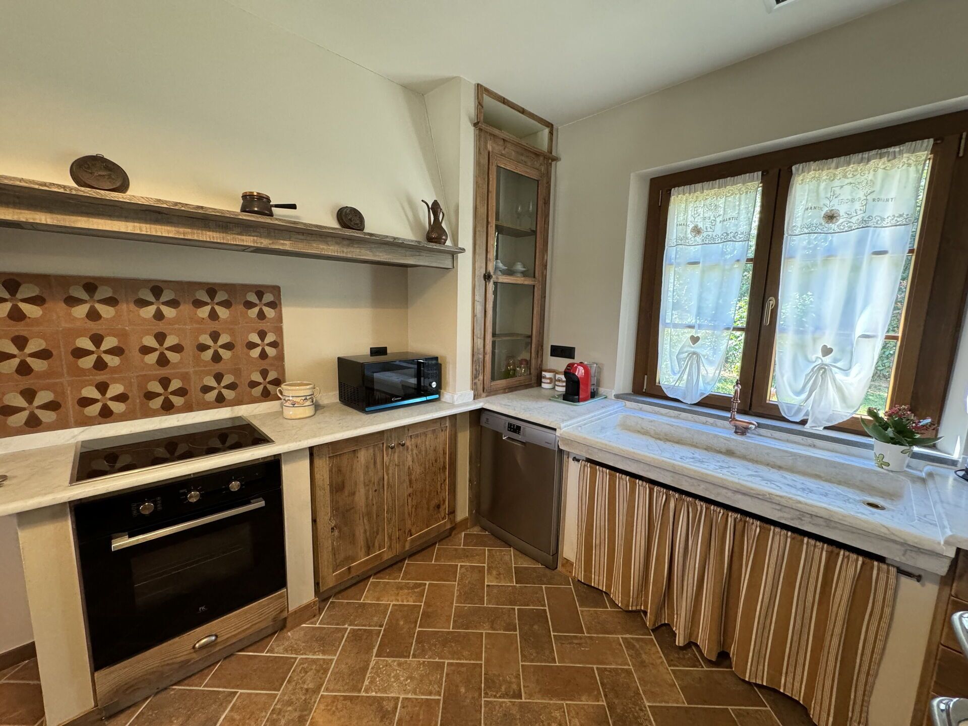 A compact kitchen with a microwave, oven, and a window with curtains.