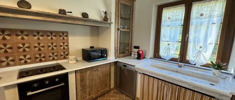 A compact kitchen with a microwave, oven, and a window with curtains.