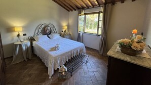A bedroom with a bed, bedside tables, a window with curtains, a wooden ceiling, and a nightstand with a candle. - Villa in Lucca with 3 bedrooms sleeps 7 (Lucca)