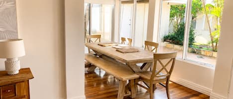 A dining area with a wooden table and benches, a lamp, and a view of greenery outside.