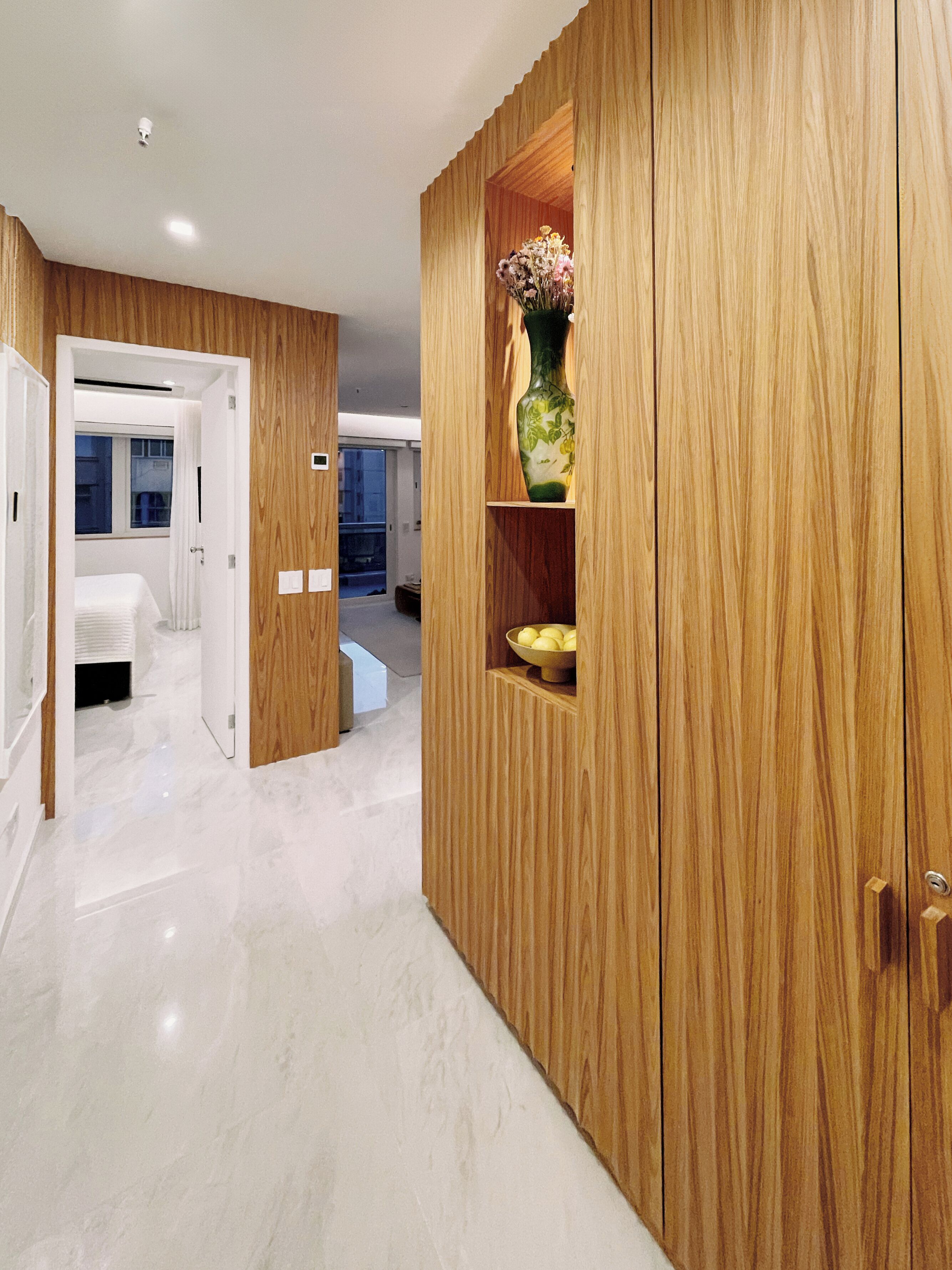 Une chambre d’hôtel moderne avec une armoire en bois, un vase de fleurs et un saladier rempli de fruits.