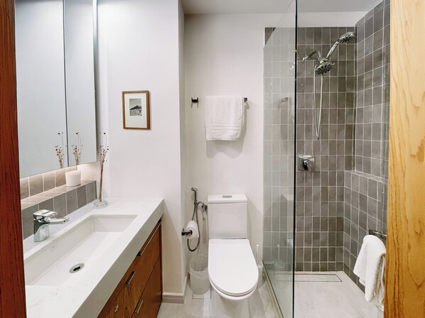Un baño moderno con cabina de ducha de vidrio, inodoro blanco y tocador con espejo.