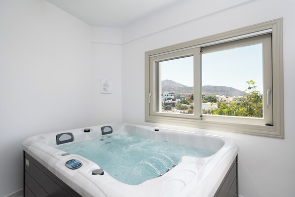 Une salle de bain moderne avec un jacuzzi, une fenêtre donnant sur un paysage urbain et un mur blanc.