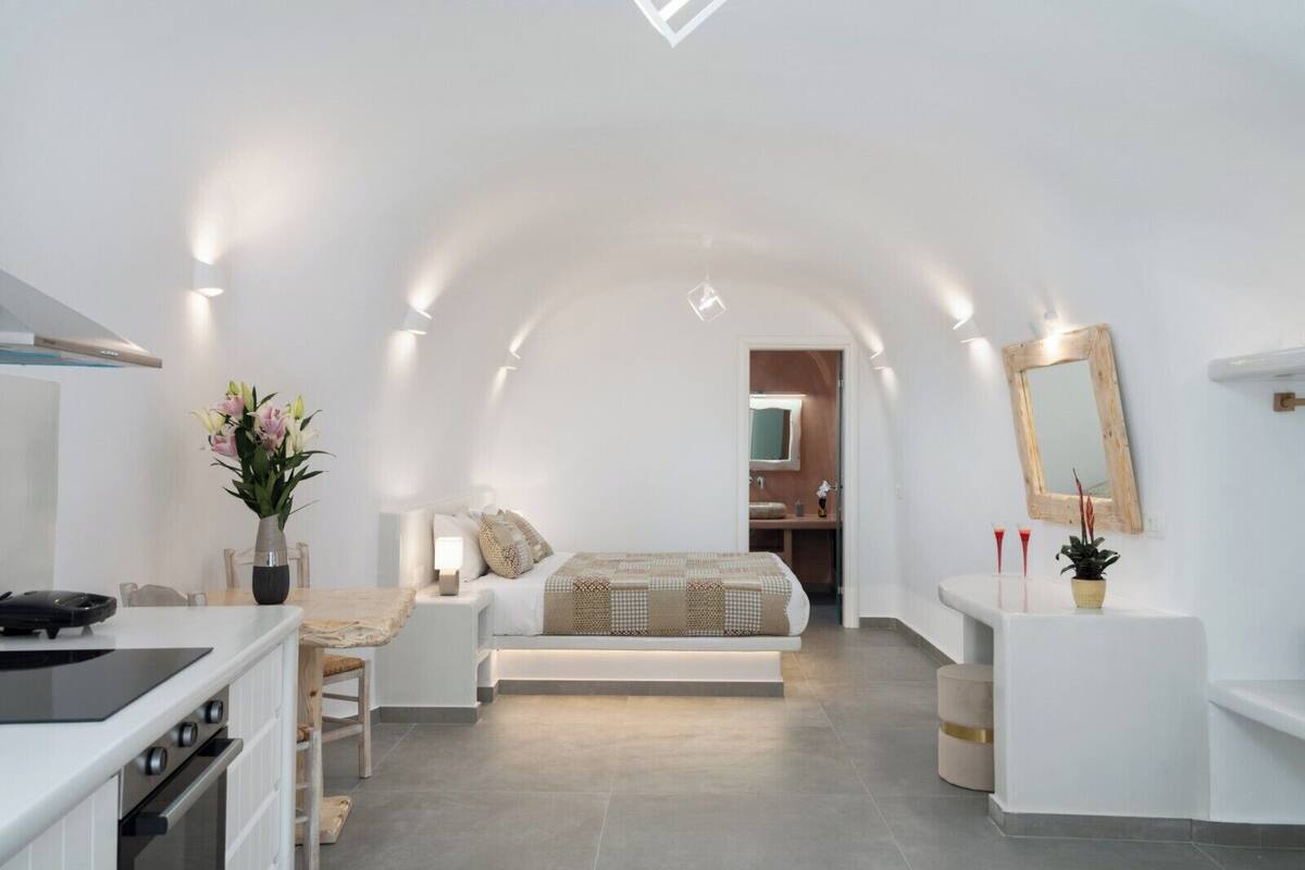 A modern, well-lit bedroom with a bed, bedside table, and a small sitting area.