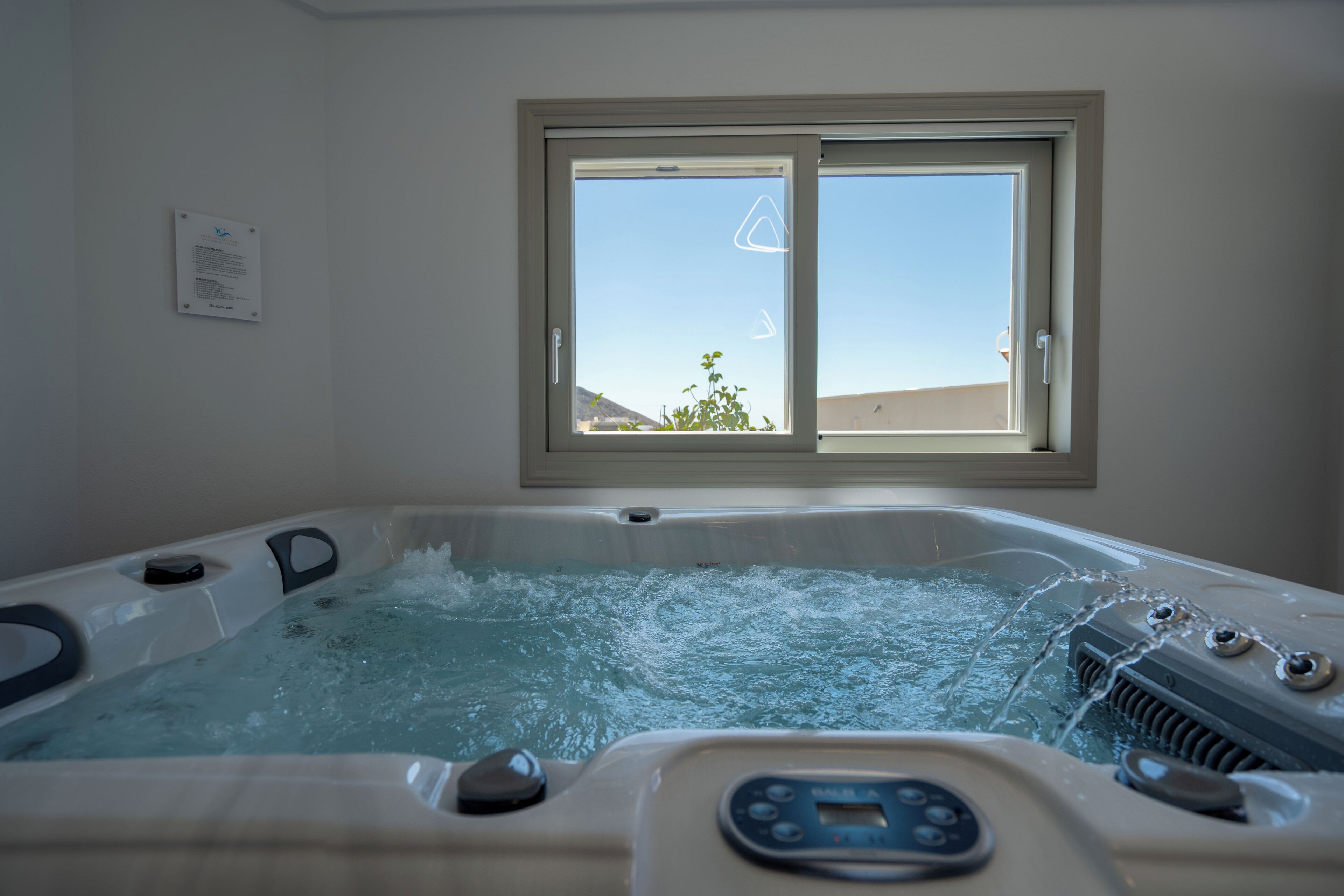 A hot tub with a control panel, a window with a view of the outdoors, and a wall-mounted sign.