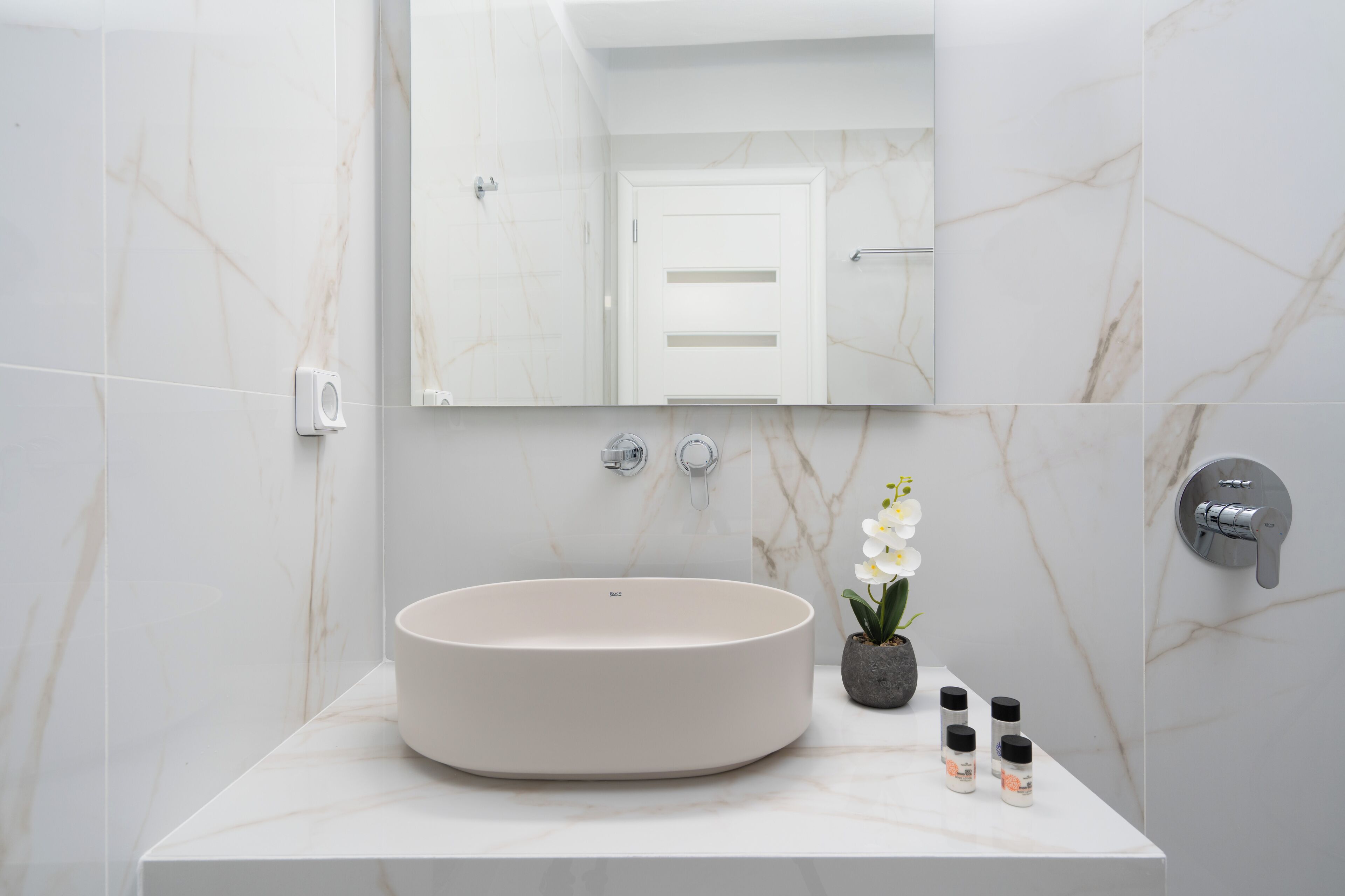 Ein modernes Badezimmer mit einem runden Waschbecken, einem Spiegel und einer Topf-Orchidee.