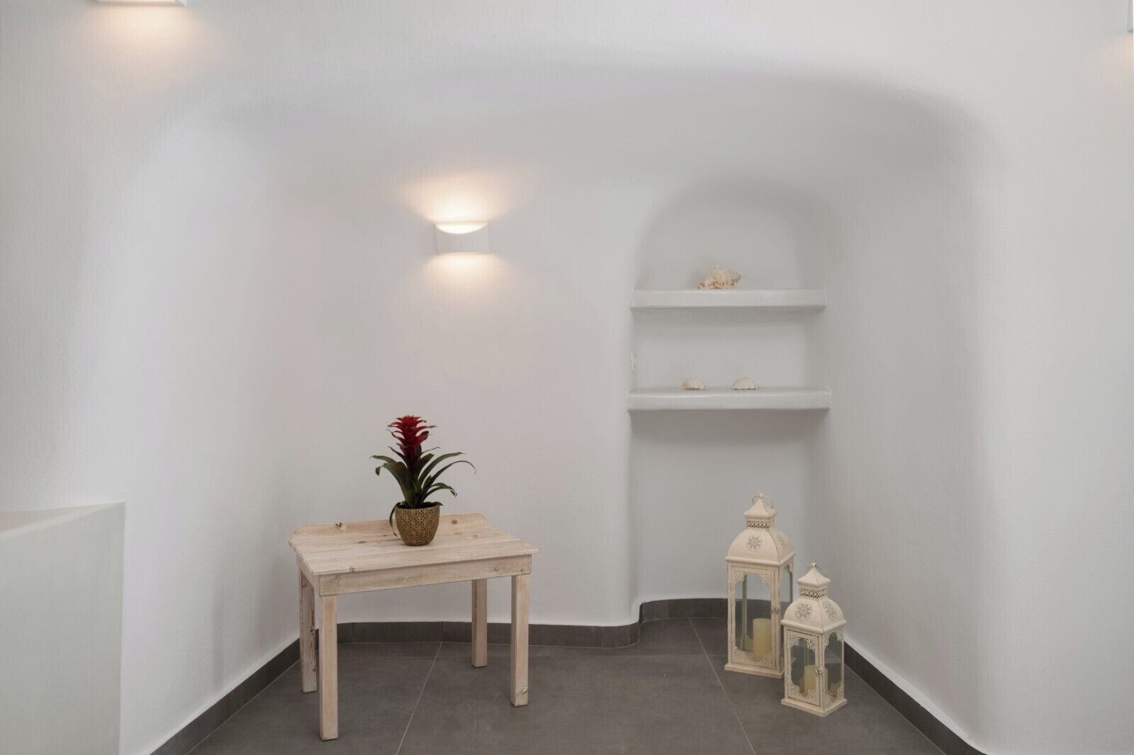 Ein schmaler Korridor mit einem Holztisch, einem Blumentopf, weißen Wänden und einem kleinen Regal mit Dekoration.