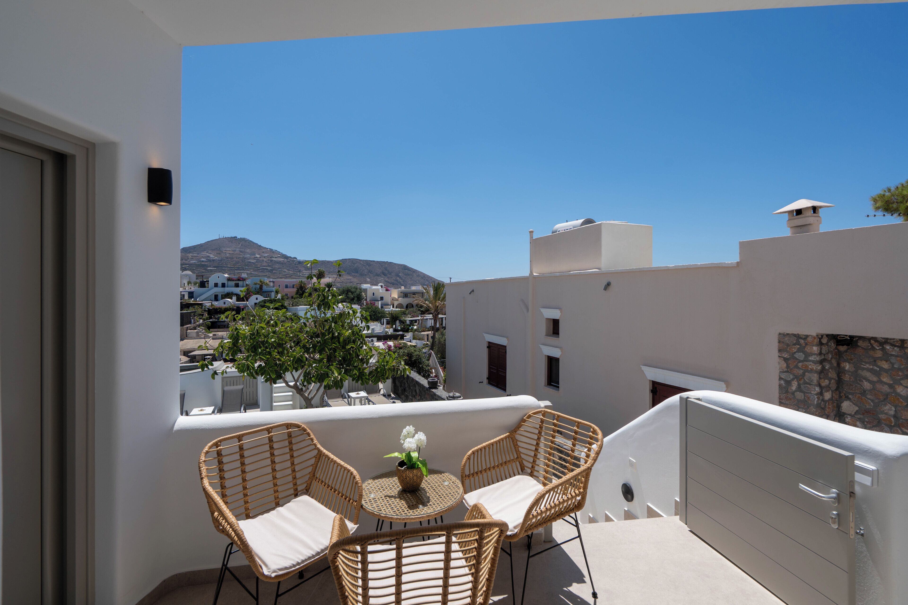 Un balcon avec des fauteuils et une table en osier, d’où l’on peut admirer une ville avec ses bâtiments et, au loin, une montagne.