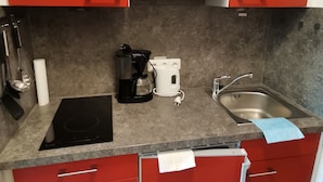Cocina compacta con gabinetes rojos, microondas, cafetera y lavamanos.