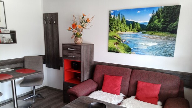 Una sala de estar moderna con un sofá rojo, una mesita de madera y una cocina con un taburete de bar.
