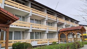 Un hotel de varios pisos con balcones, una pérgola de madera y un letrero que indica un restaurante.