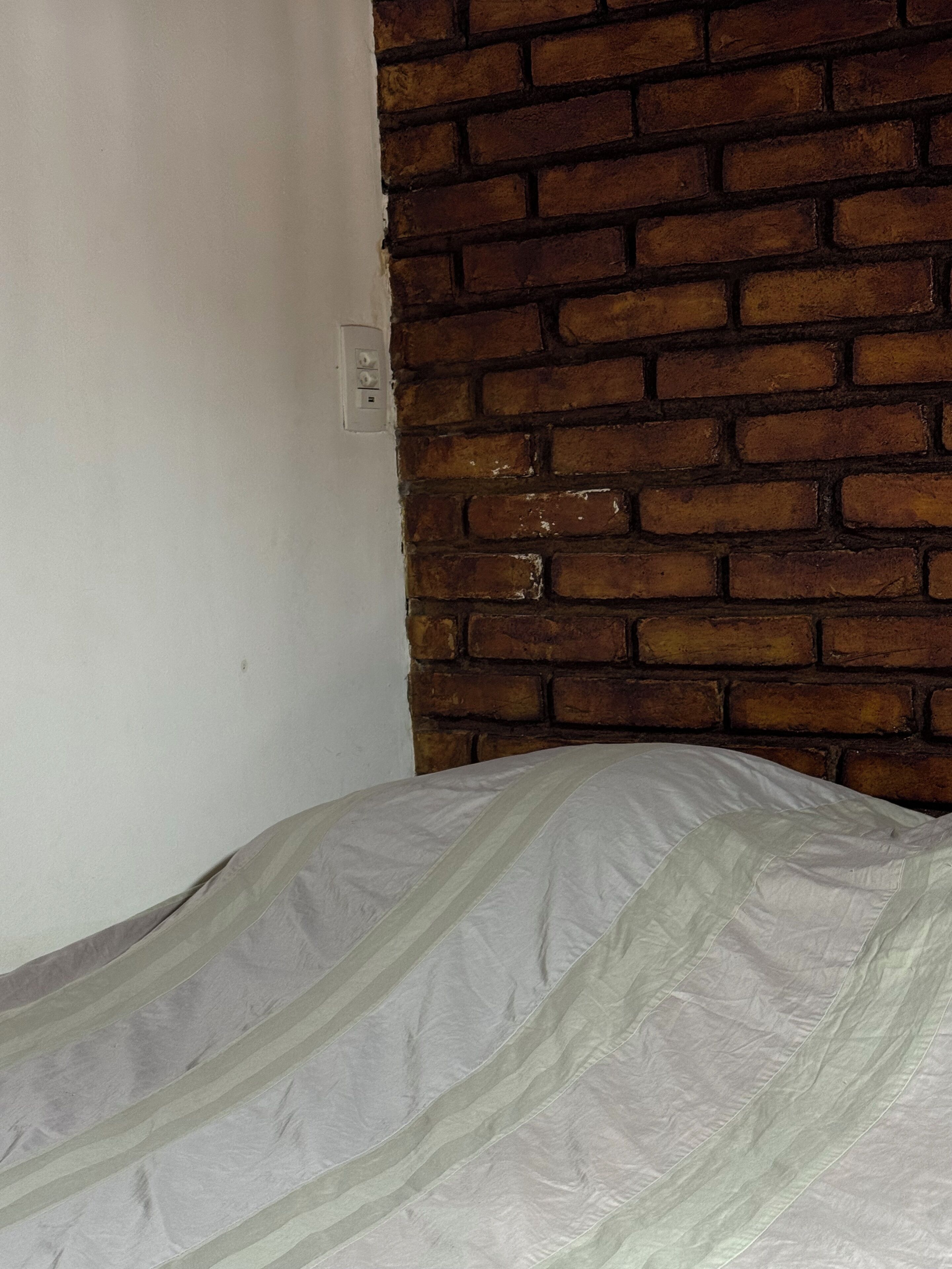 A room with a brick wall and a bed with a striped sheet.