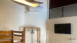 A room with a wooden chair, a table, a TV mounted on the wall, and a ceiling fan. - Home Beach Mar (Aquiraz)