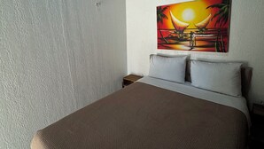 A hotel room with a bed, a painting of a sunset, an air conditioner, and a nightstand. - Home Beach Mar (Aquiraz)