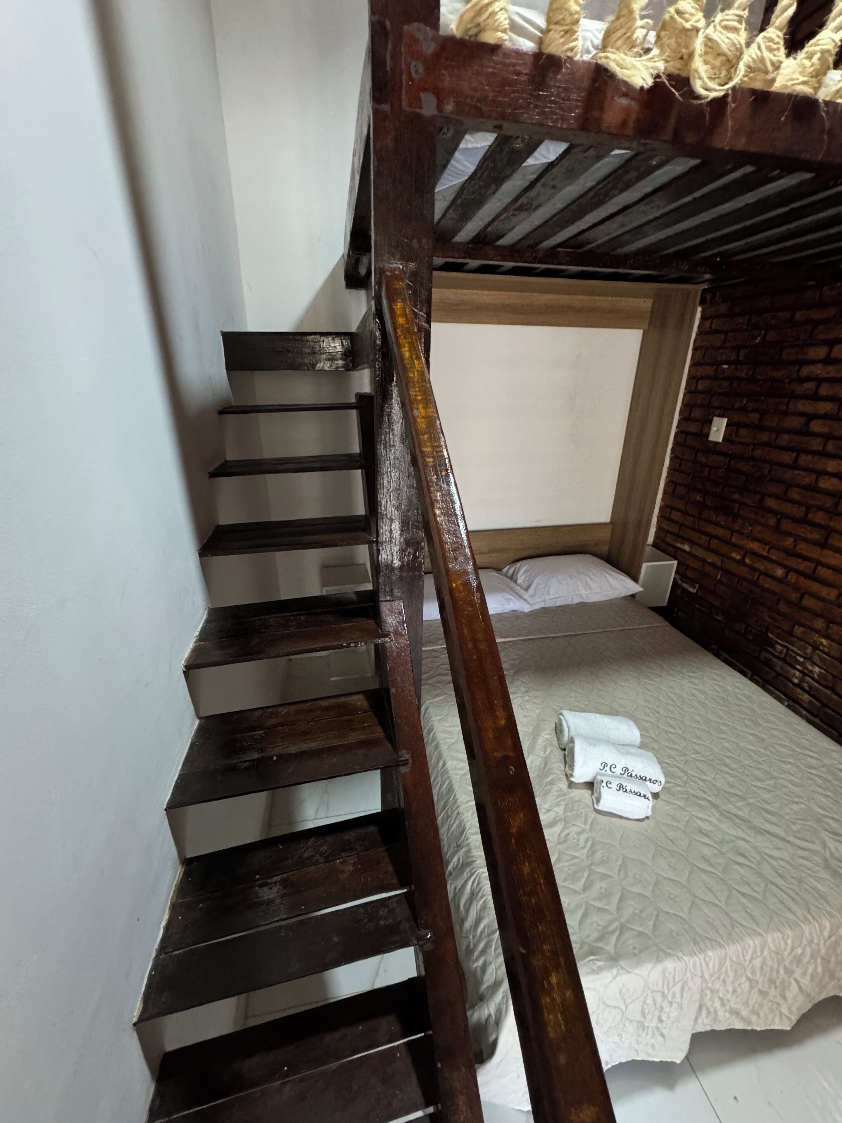A bunk bed with a wooden ladder, a single bed with a white quilt, and a brick wall.