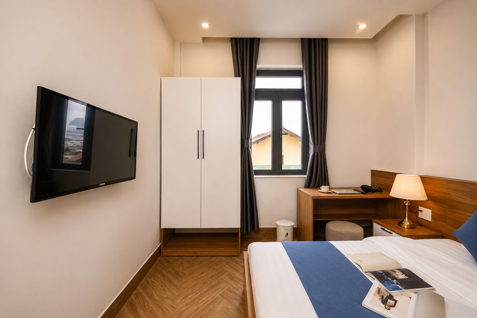 Habitación de hotel con cama, escritorio, silla, televisión, armario y ventana con cortinas.