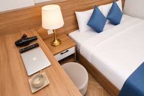 A hotel room with a wooden headboard, a bed with white bedding and blue pillows, a bedside table with a lamp, a laptop, a remote control, and a cup. - Yen Lam Villa Hotel (Xuan Truong - Da Lat)