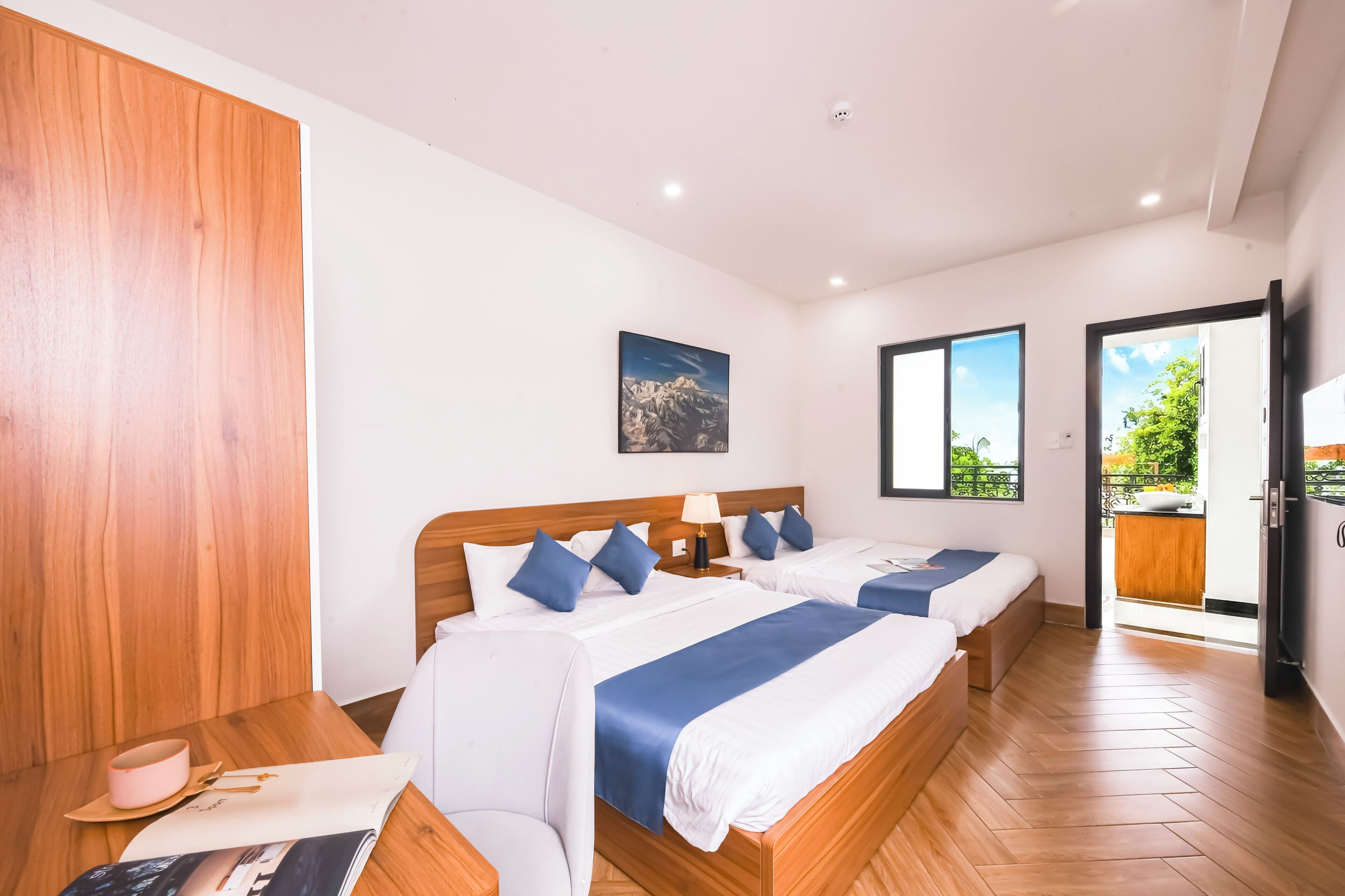 Habitación de hotel con dos camas, un armario de madera, un cuadro en la pared y vistas al exterior a través de las ventanas.