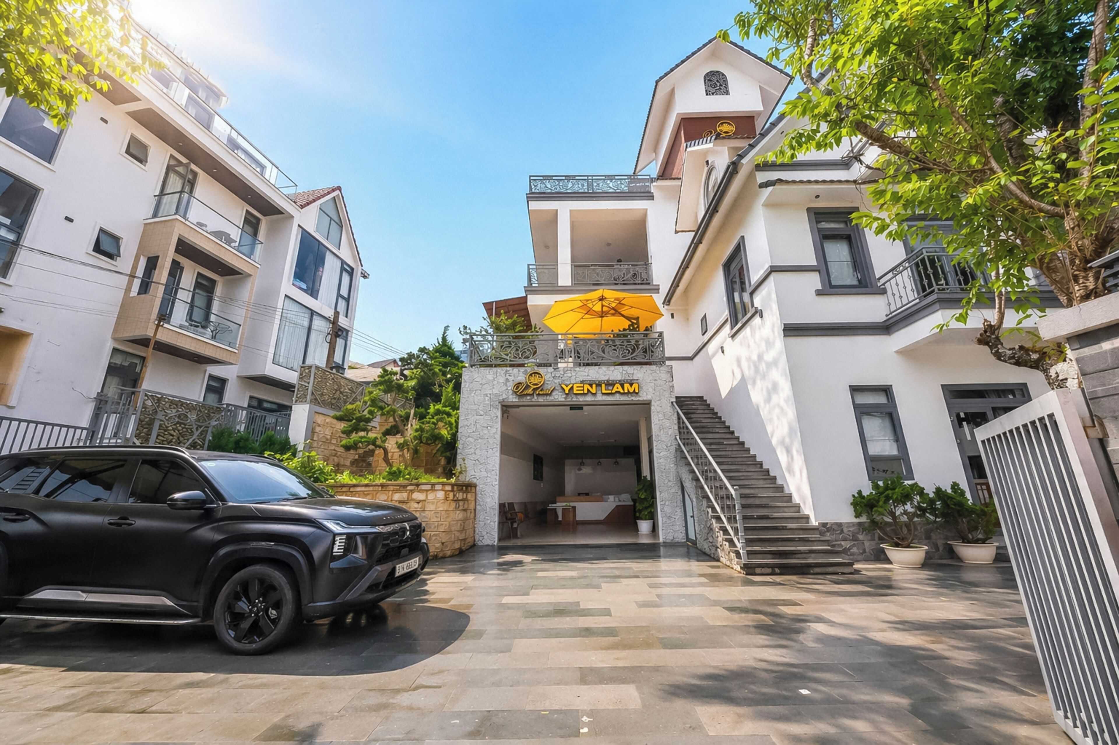 A hotel entrance with a staircase leading to the second floor, a parked SUV, and a clear sky.