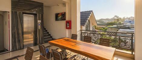 A dining area with a wooden table and chairs, a staircase, and a view of buildings through a balcony railing.